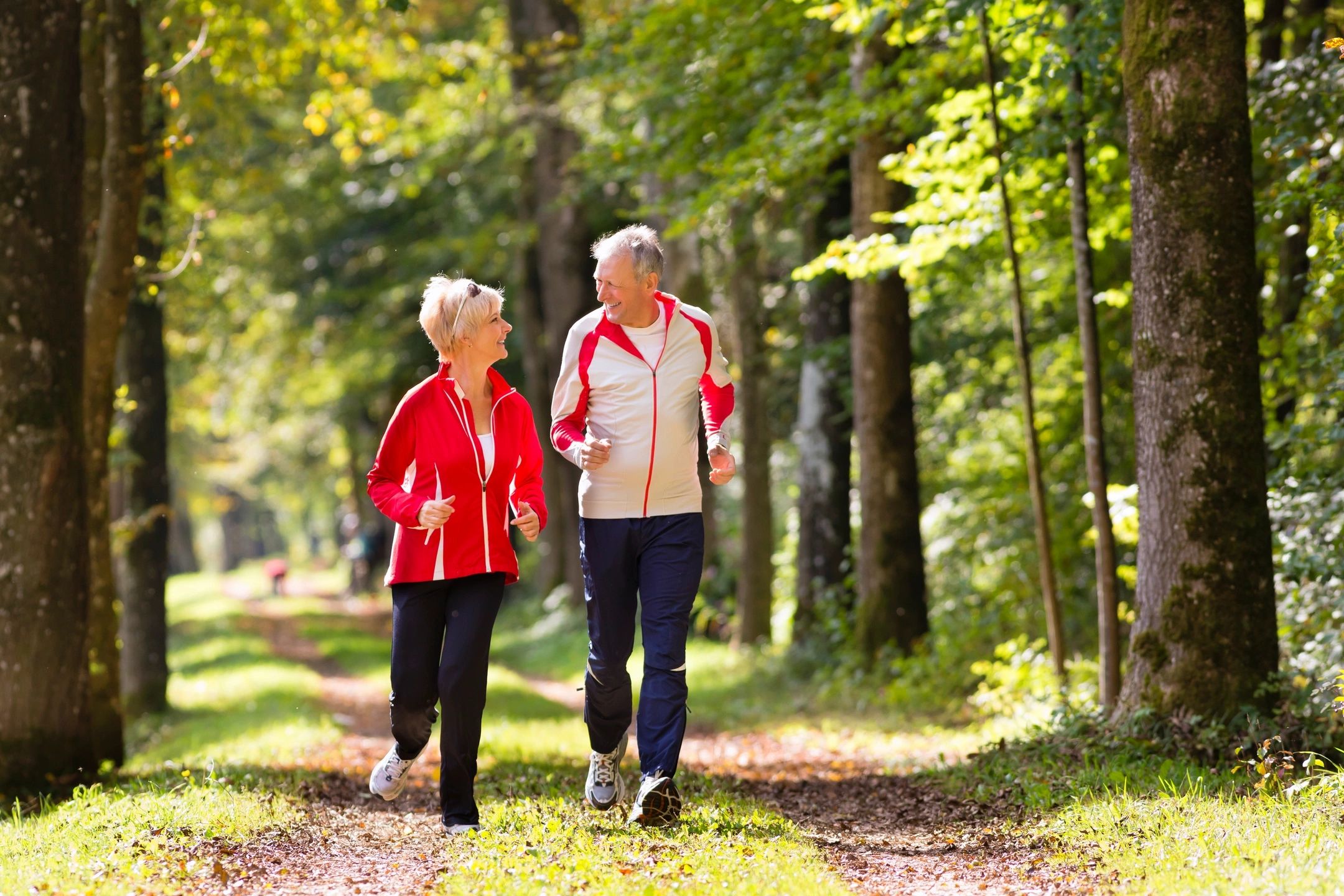 Elderly couple walking together in a sunny forest path.