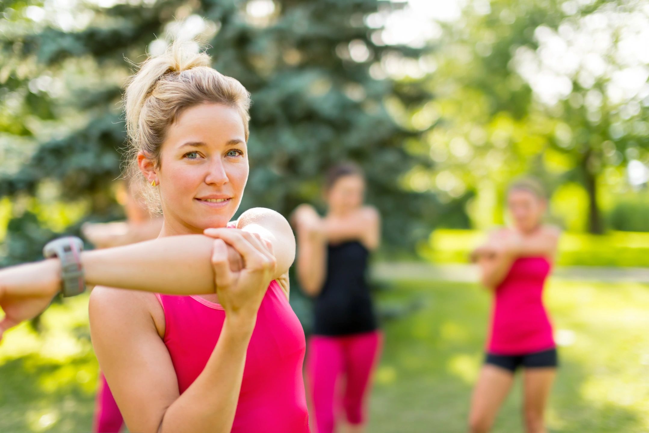 Women exercising outdoors, stretching their arms.