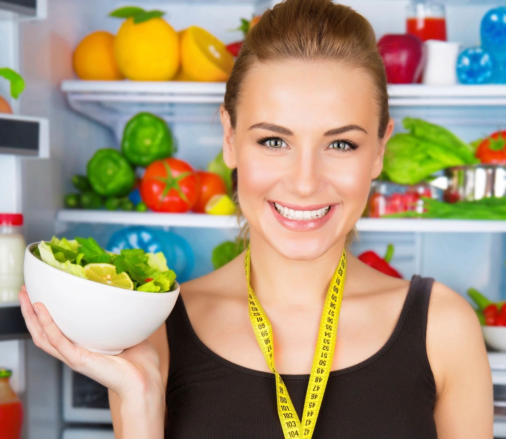 Smiling woman holding a bowl of salad in a colorful kitchen.