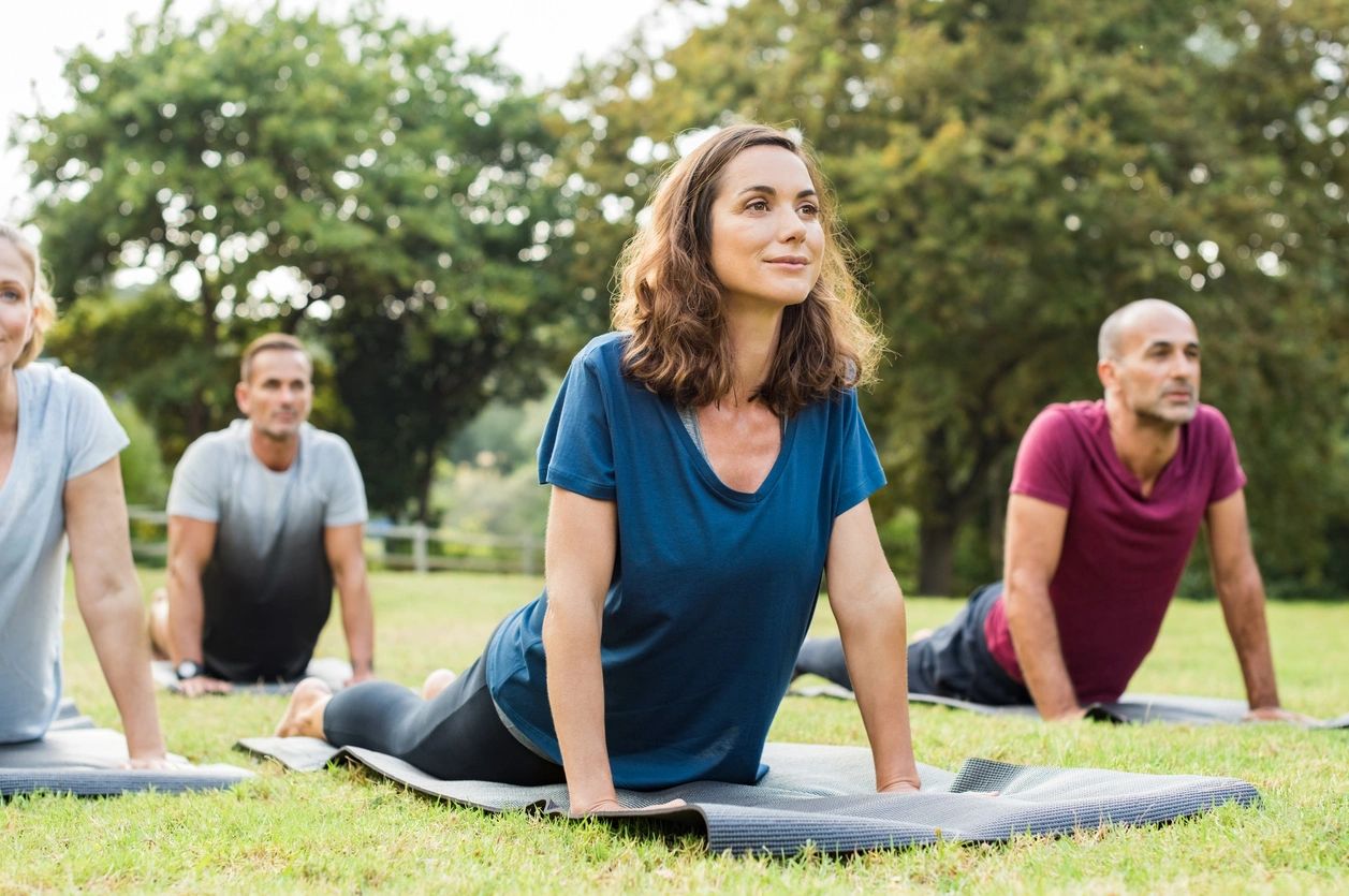 Group practicing yoga outdoors on mats, focusing on upward dog pose.